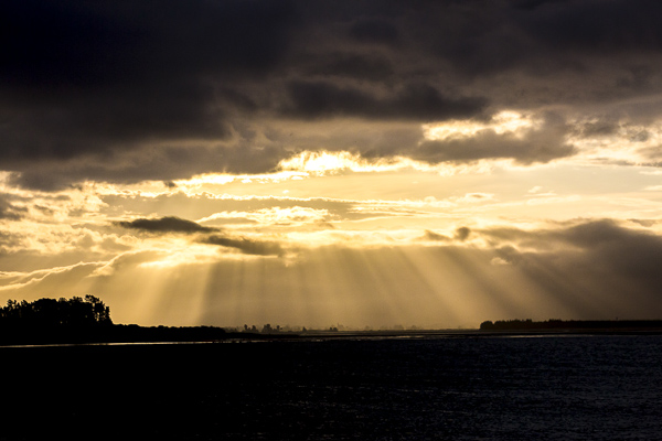 Light is filtered though the clouds at sunset over beautiful Tahanui beach in Nelson, New Zealand.